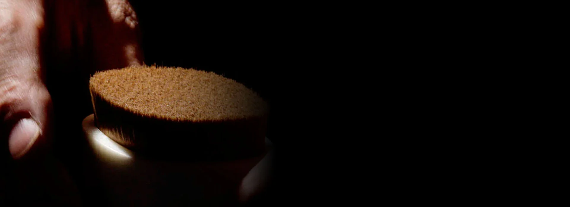 alt="A dramatic, artistic close-up of a hand holding a dense Shu Uemura foundation brush, with a single light source highlighting the texture of the bristles."